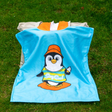 Badeponcho i sterke farger. Ligger over en bag på gresset.