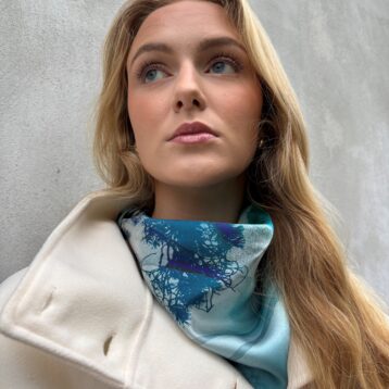 Kvinne med blondt hår og blått silkesjal. Grå bakgrunn.