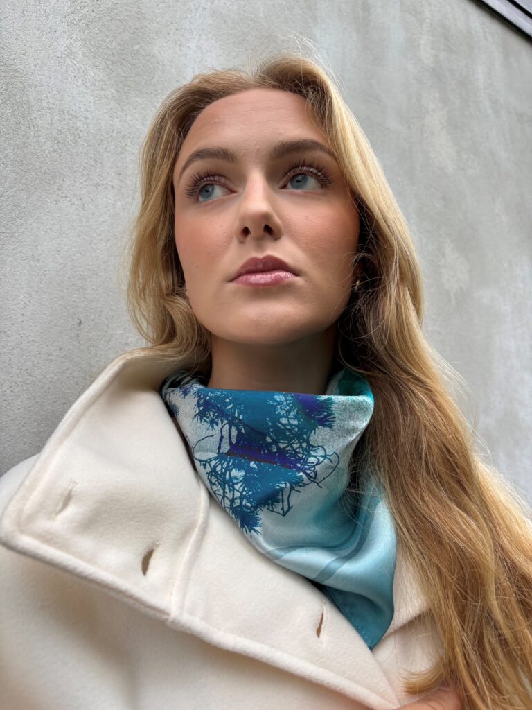 Kvinne med blondt hår og blått silkesjal. Grå bakgrunn.