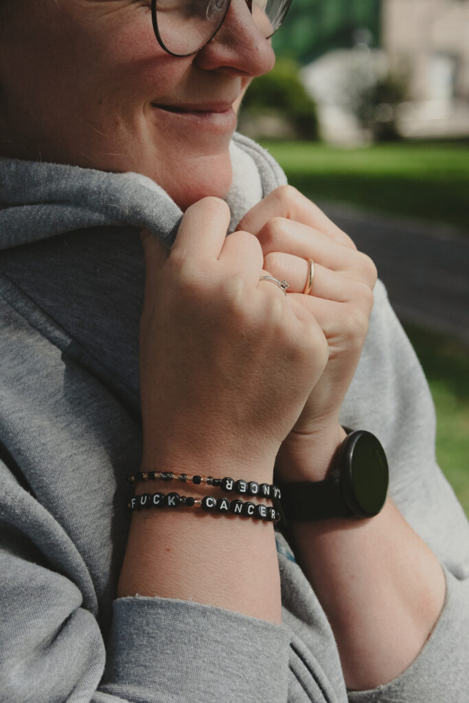 Perlearmbånd på en kvinnes håndledd. Kvinnen holder i kragen på hettegenseren sin.